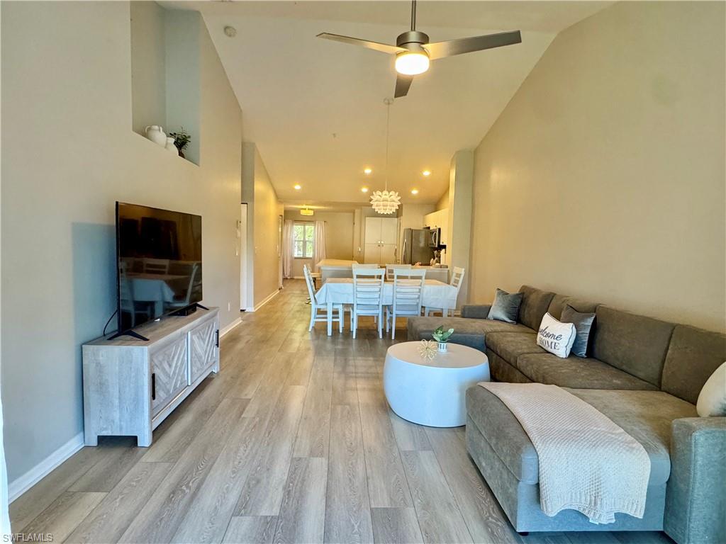 Living room with wood finished floors, high vaulted ceiling, and a ceiling fan