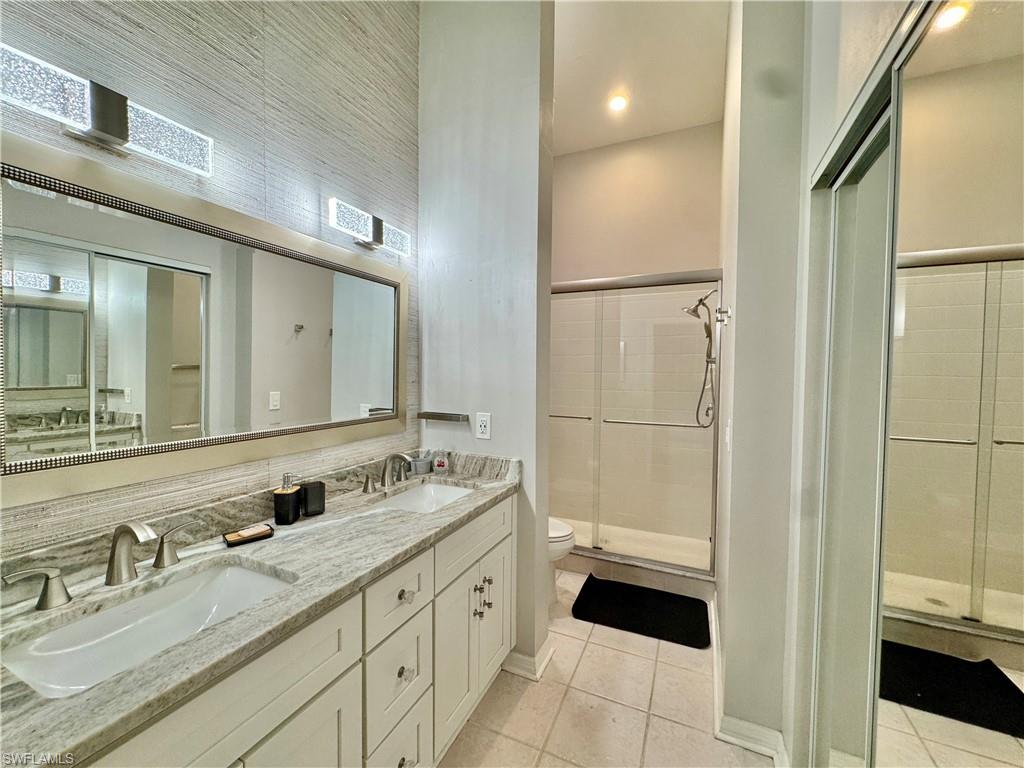Bathroom featuring a shower stall, double vanity, and light tile patterned flooring