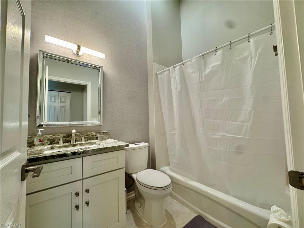 Bathroom with shower / tub combo, vanity, light tile patterned floors, and a textured wall