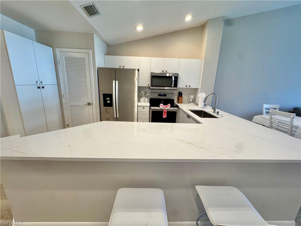 Kitchen featuring a kitchen bar, a peninsula, appliances with stainless steel finishes, lofted ceiling, and white cabinetry