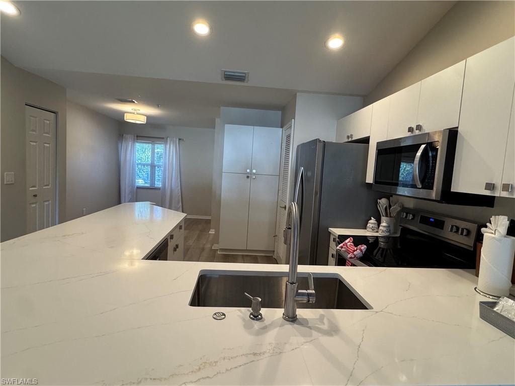 Kitchen featuring appliances with stainless steel finishes, recessed lighting, dark wood-style flooring, white cabinetry, and light stone countertops