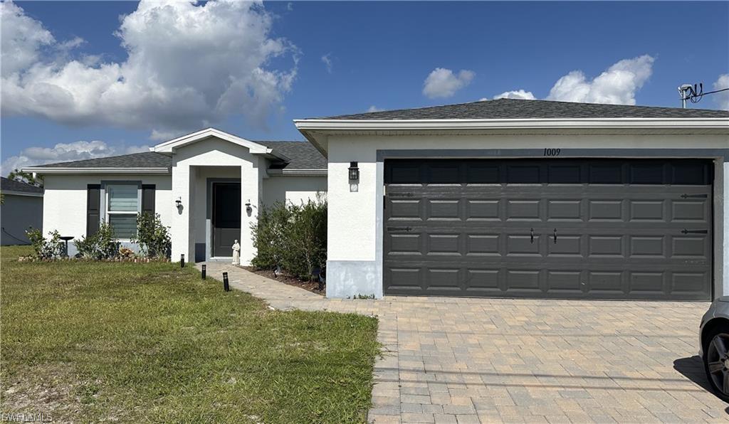 Ranch-style house featuring decorative driveway, a front lawn, stucco siding, an attached garage, and roof with shingles