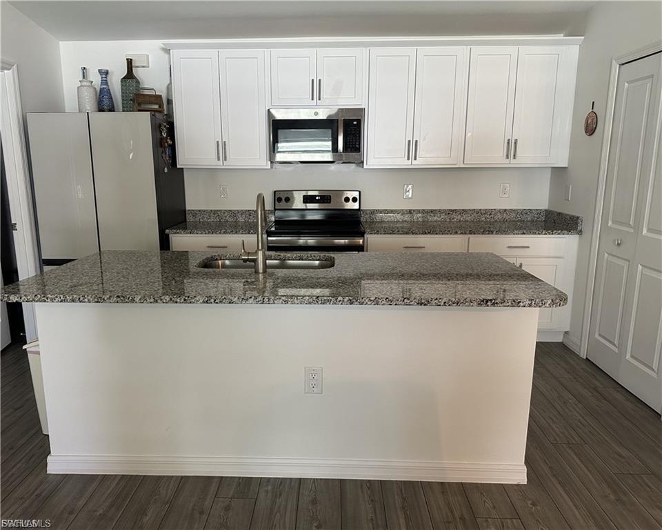 Kitchen featuring white cabinetry, stainless steel appliances, dark stone countertops, and dark wood finished floors