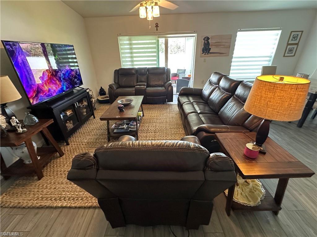 Living room with ceiling fan, light wood finished floors, and vaulted ceiling