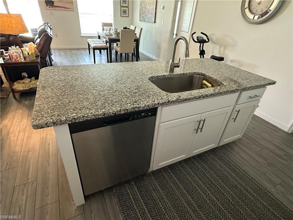 Kitchen featuring a center island with sink, dark wood finished floors, white cabinetry, dishwasher, and open floor plan