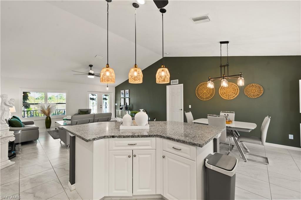 Kitchen featuring hanging light fixtures, white cabinets, light stone counters, a center island, and open floor plan