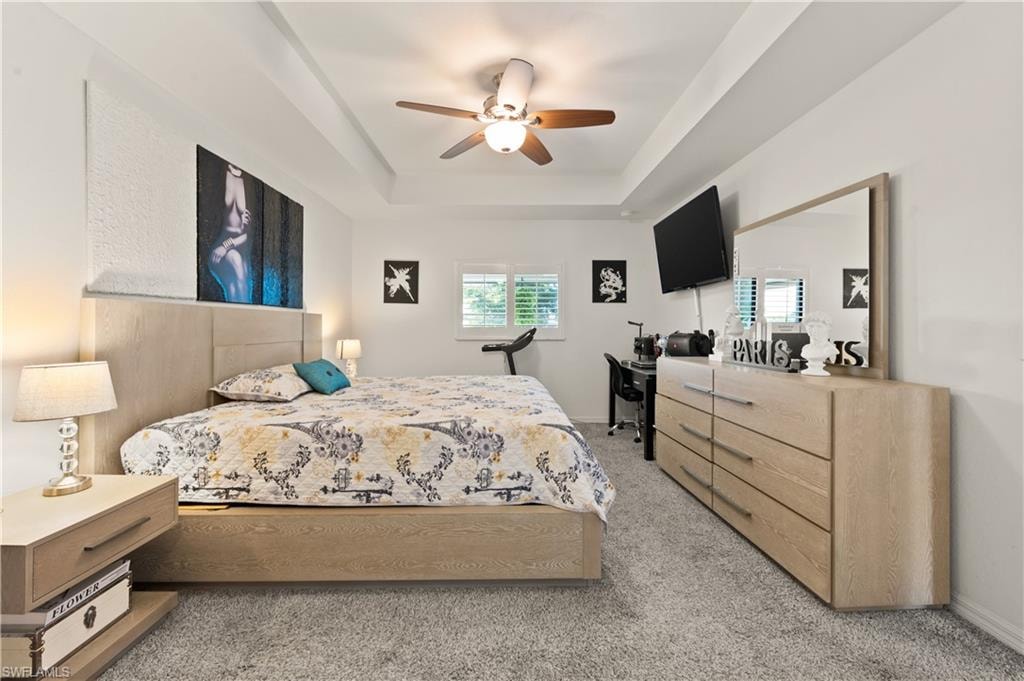 Bedroom featuring a raised ceiling, ceiling fan, and light colored carpet