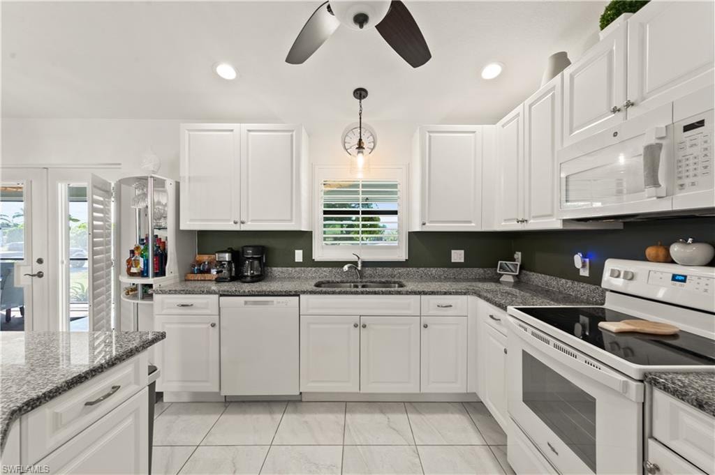 Kitchen featuring white appliances, white cabinetry, dark stone counters, pendant lighting, and a ceiling fan