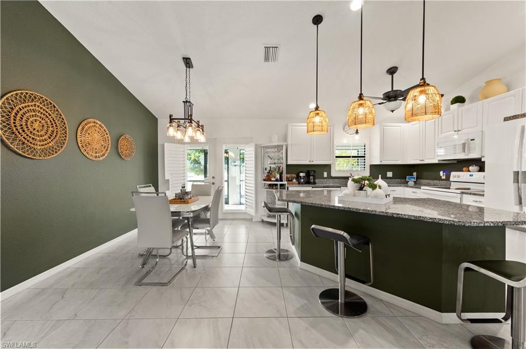 Kitchen with vaulted ceiling, dark stone counters, pendant lighting, white cabinetry, and a kitchen breakfast bar