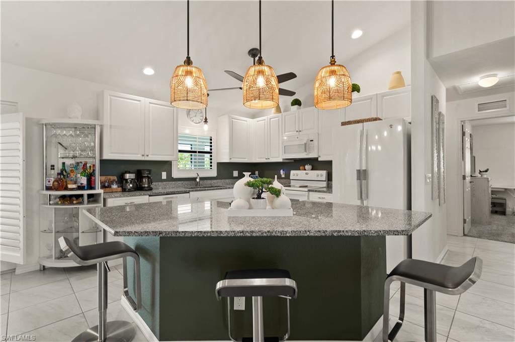 Kitchen featuring a breakfast bar, decorative light fixtures, white cabinets, dark stone countertops, and lofted ceiling