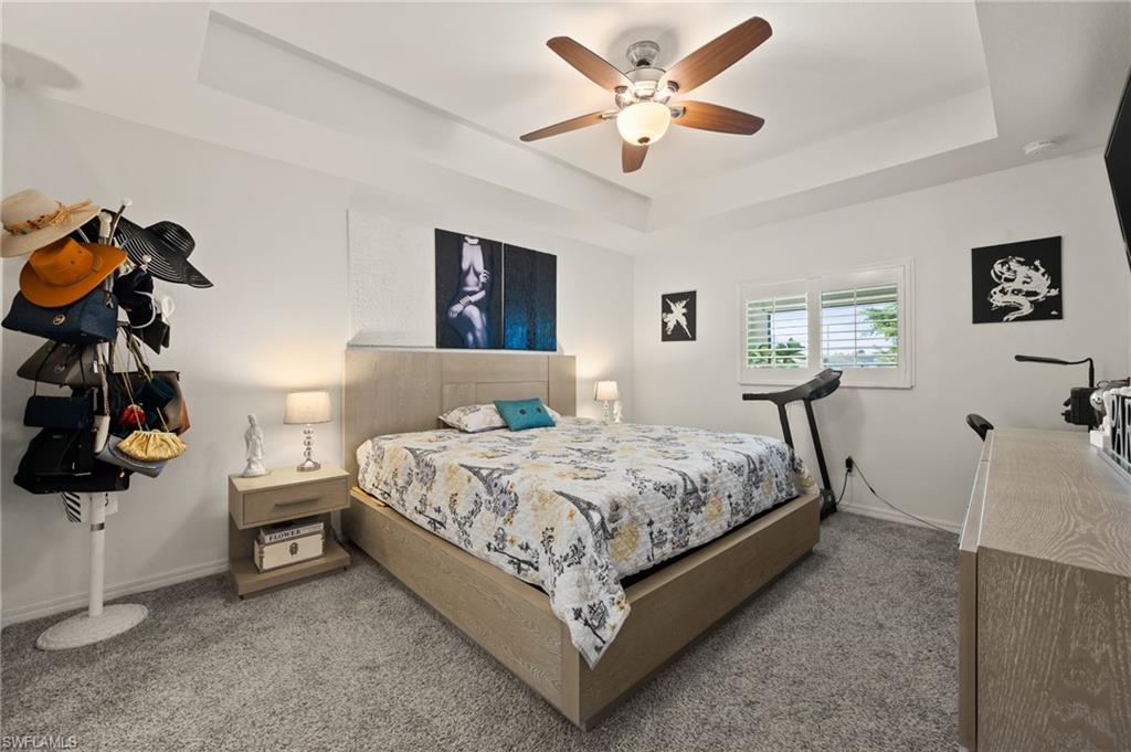 Bedroom featuring a ceiling fan, carpet flooring, and a tray ceiling