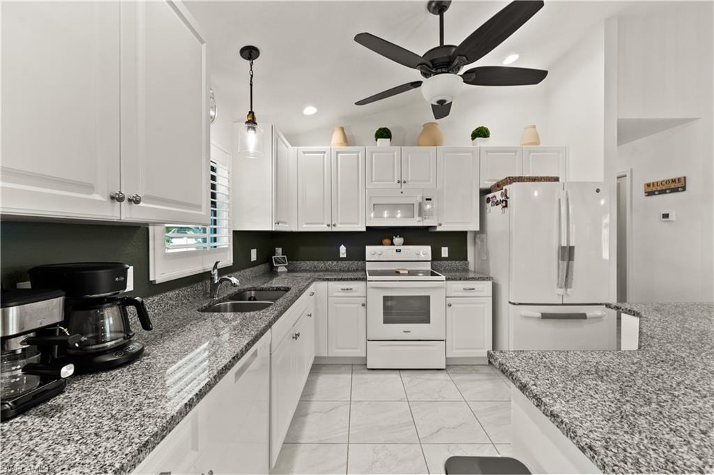 Kitchen featuring white appliances, lofted ceiling, dark stone counters, white cabinetry, and recessed lighting