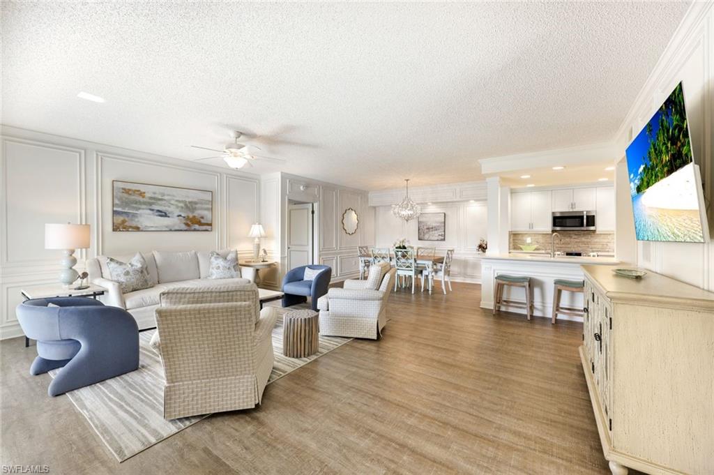 Living area featuring a decorative wall, a textured ceiling, a ceiling fan, light wood-style floors, and crown molding