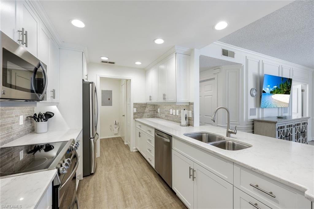 Kitchen featuring stainless steel appliances, white cabinets, light stone counters, light wood-type flooring, and a textured ceiling
