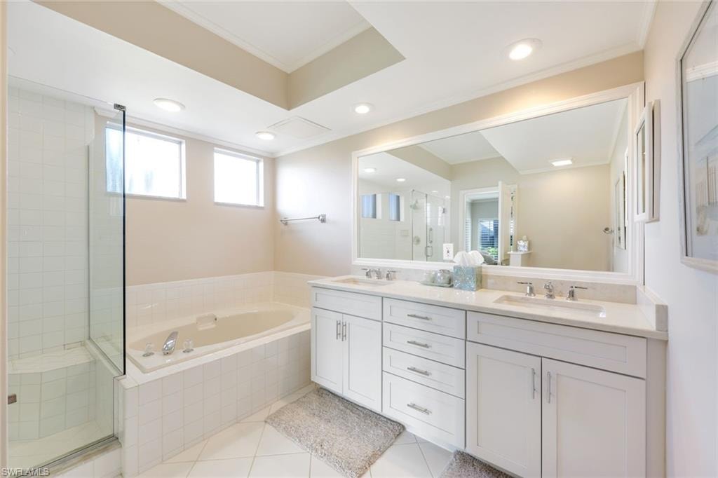 Full bath featuring a stall shower, crown molding, light tile patterned flooring, double vanity, and a garden tub