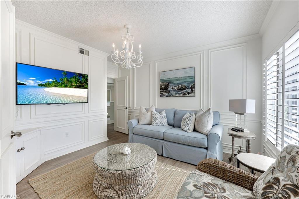 Living room with a decorative wall, a textured ceiling, a chandelier, wood finished floors, and ornamental molding