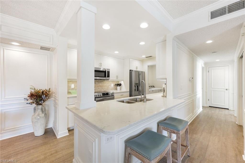 Kitchen with a textured ceiling, crown molding, a decorative wall, white cabinets, and light wood-style flooring