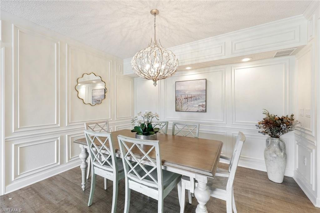 Dining area featuring a decorative wall, a chandelier, light wood-type flooring, and a textured ceiling