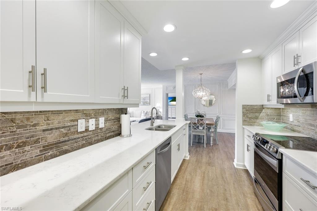 Kitchen featuring stainless steel appliances, backsplash, white cabinets, light stone counters, and light wood-type flooring