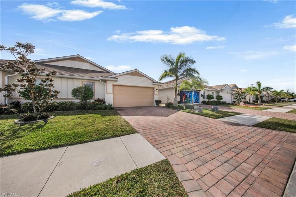 Ranch-style home featuring decorative driveway, an attached garage, a front yard, a residential view, and board and batten siding