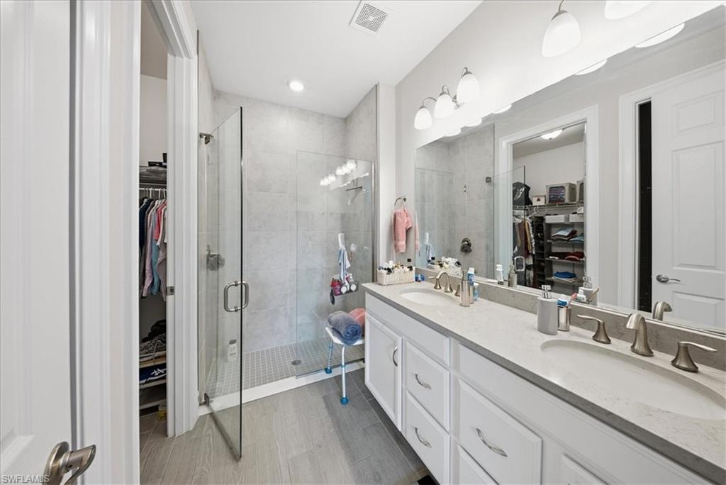 Full bathroom with a walk in closet, double vanity, and a stall shower