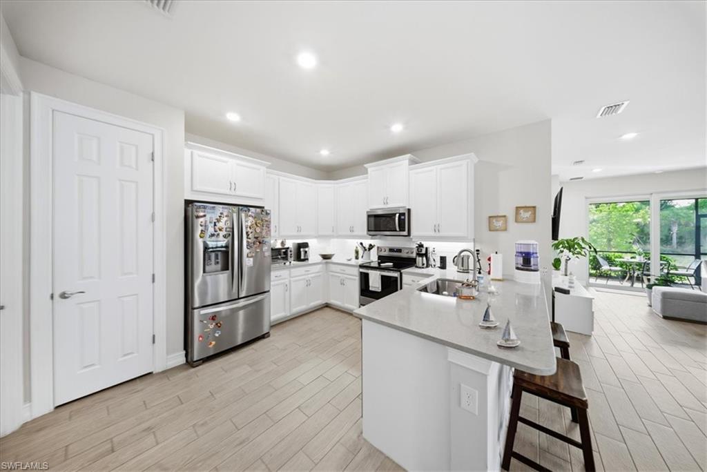 Kitchen featuring appliances with stainless steel finishes, a breakfast bar area, a peninsula, white cabinets, and light stone countertops