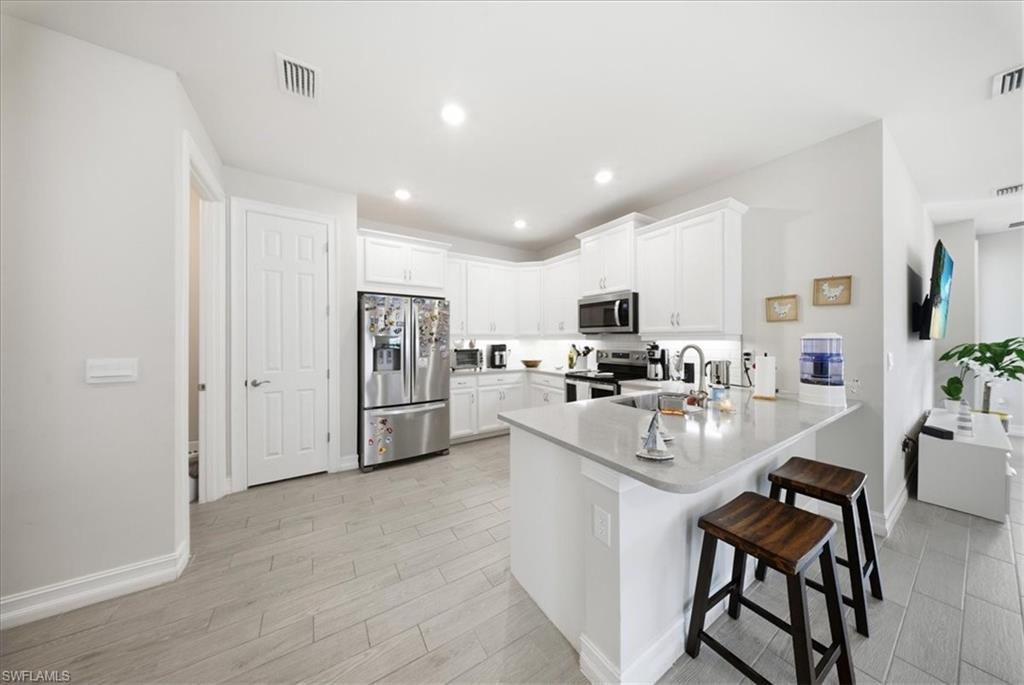 Kitchen featuring appliances with stainless steel finishes, a kitchen bar, white cabinets, a peninsula, and wood finish floors