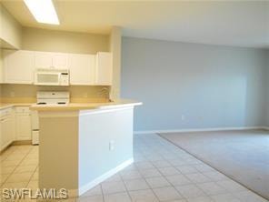 Kitchen with white cabinetry, light countertops, white appliances, light tile patterned flooring, and a peninsula