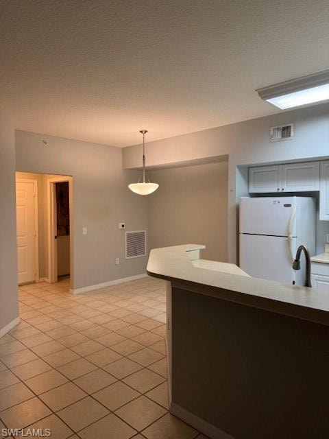 Kitchen with light countertops, fridge, decorative light fixtures, a textured ceiling, and light tile patterned flooring