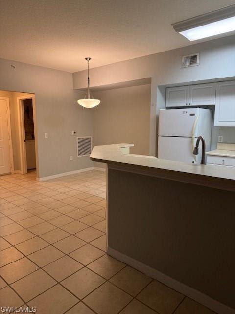 Kitchen with light countertops, refrigerator, decorative light fixtures, light tile patterned floors, and white cabinets