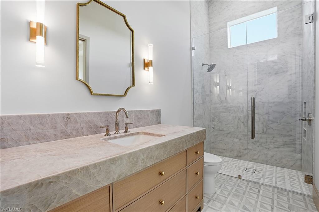 Bathroom featuring a natural stone vanity with an integrated sink, a large mirror with a gold frame, and a glass-enclosed shower with a marble tile surround