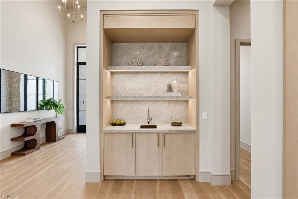 Built-in wet bar featuring a light wood-finish cabinet, integrated sink, stone countertop, and illuminated stone backsplash