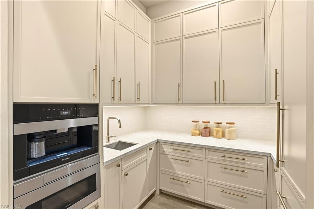 Pantry featuring coffee maker, microwave drawer, light quartz counters, tasteful tile backsplash, and light wood-style floors
