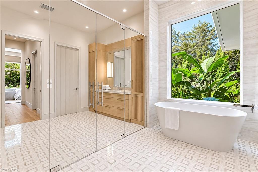 Freestanding soaking tub positioned before a large window with lush foliage