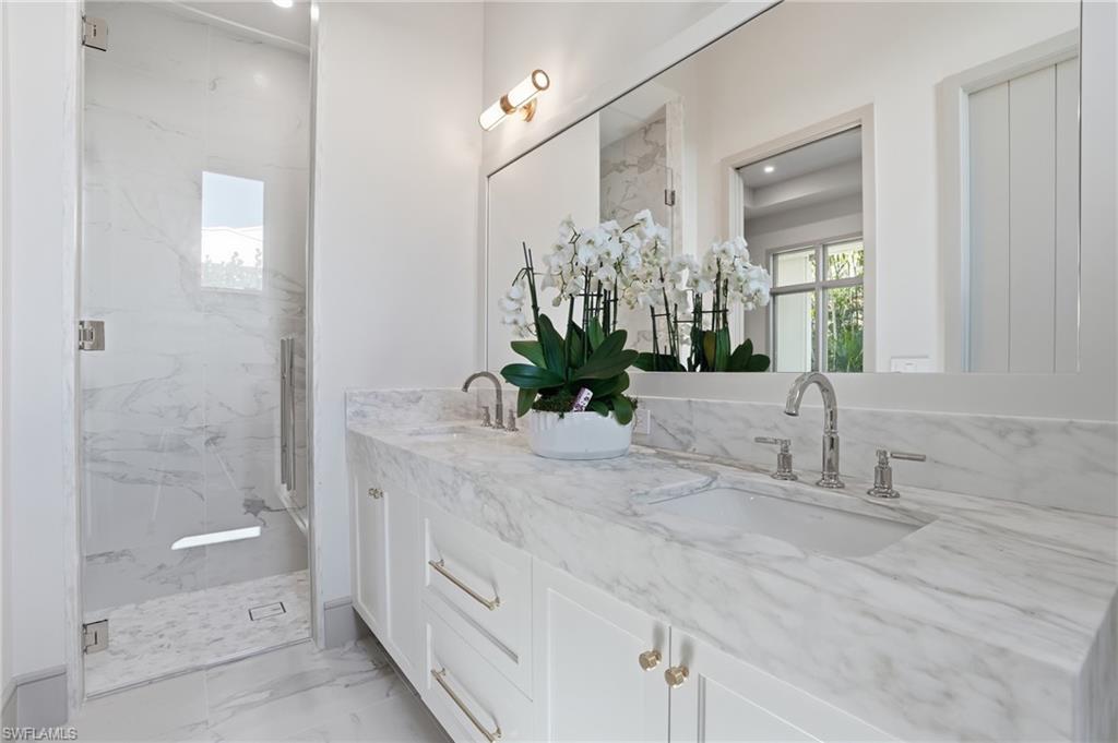 Full bathroom with double vanity, a marble finish shower, and light marble finish flooring