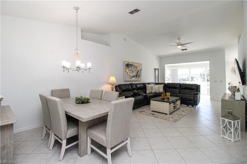 Tiled dining area with ceiling fan with notable chandelier and lofted ceiling