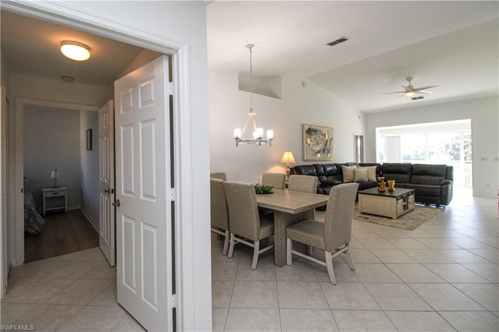 Dining area featuring ceiling fan with notable chandelier, light tile patterned floors, and lofted ceiling