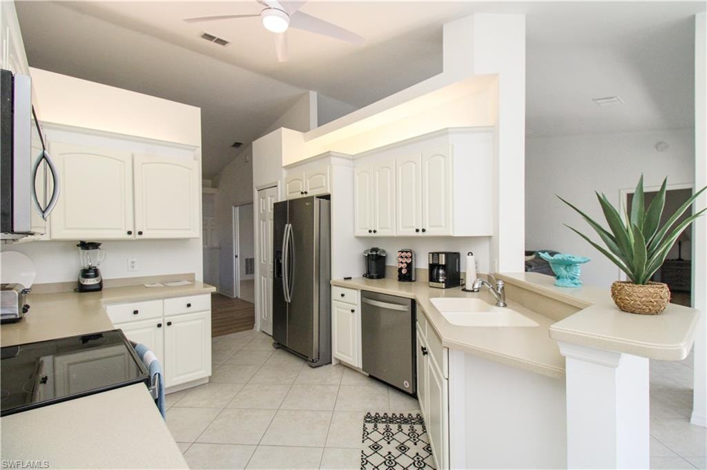 Kitchen featuring kitchen peninsula, stainless steel appliances, ceiling fan, sink, and white cabinets