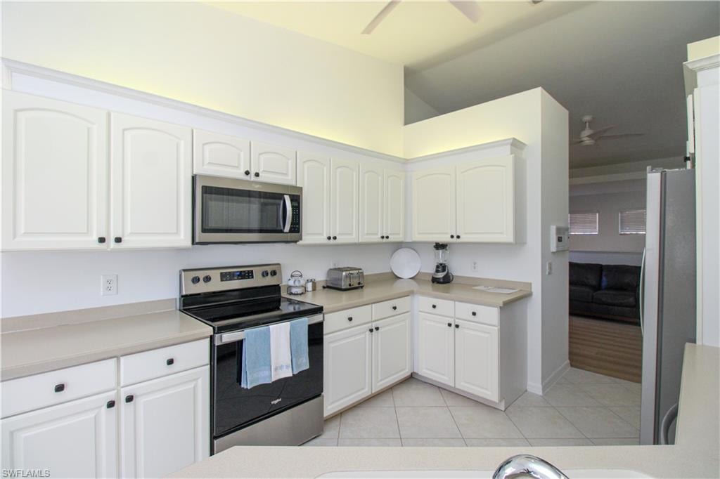 Kitchen featuring light tile patterned floors, white cabinets, stainless steel appliances, and vaulted ceiling