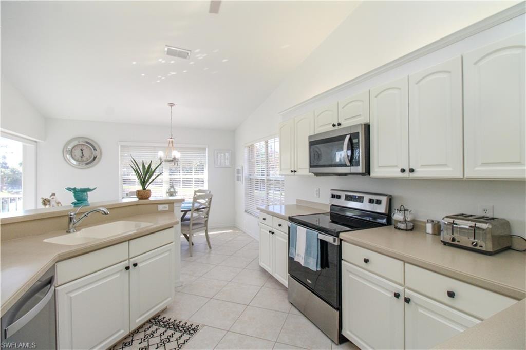 Kitchen with appliances with stainless steel finishes, vaulted ceiling, sink, decorative light fixtures, and white cabinetry
