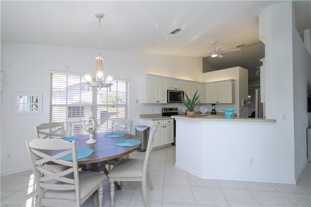 Kitchen with light tile patterned floors, ceiling fan with notable chandelier, vaulted ceiling, and pendant lighting