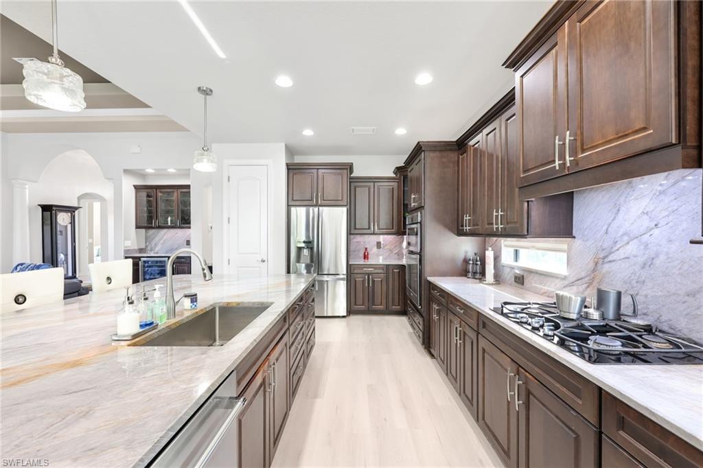 Kitchen featuring decorative light fixtures, appliances with stainless steel finishes, arched walkways, light stone counters, and dark brown cabinetry
