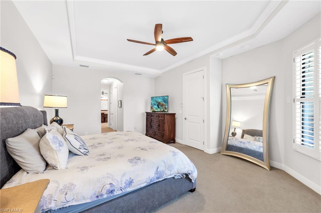 Bedroom with light colored carpet, arched walkways, a ceiling fan, a tray ceiling, and ensuite bath