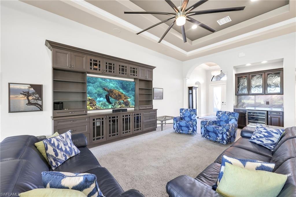 Carpeted living area with arched walkways, a bar, wine cooler, a raised ceiling, and recessed lighting