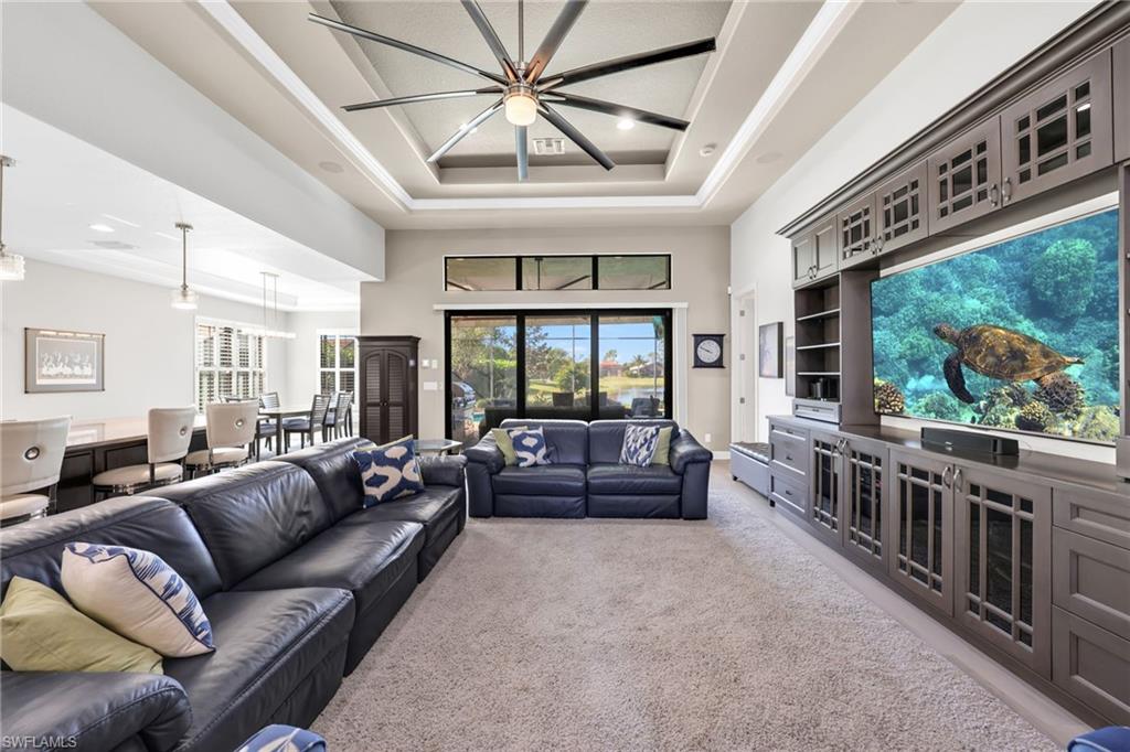 Living room with light colored carpet, a raised ceiling, and a high ceiling