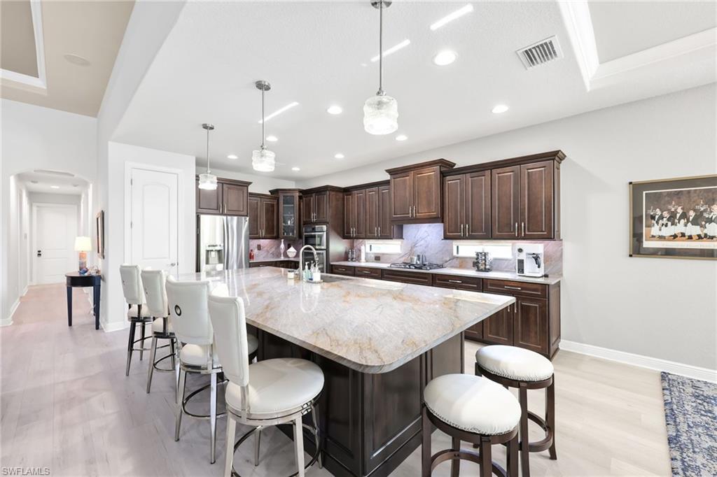 Kitchen with dark brown cabinetry, a kitchen breakfast bar, hanging light fixtures, arched walkways, and recessed lighting
