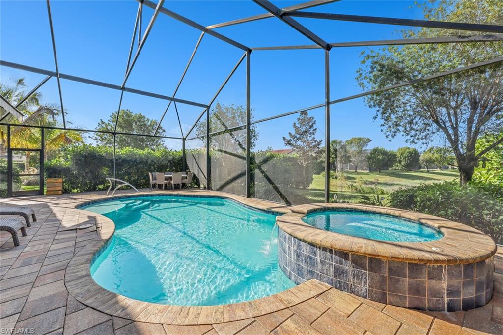 View of swimming pool featuring a pool with connected hot tub, glass enclosure, a sunroom, and a patio area