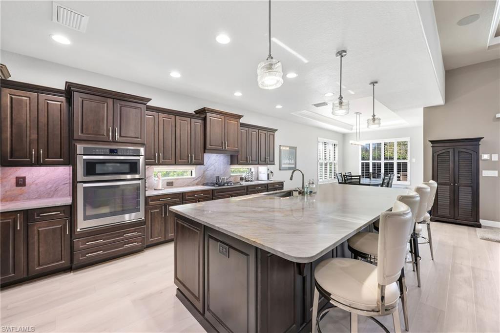 Kitchen featuring dark brown cabinetry, a raised ceiling, a center island with sink, pendant lighting, and recessed lighting