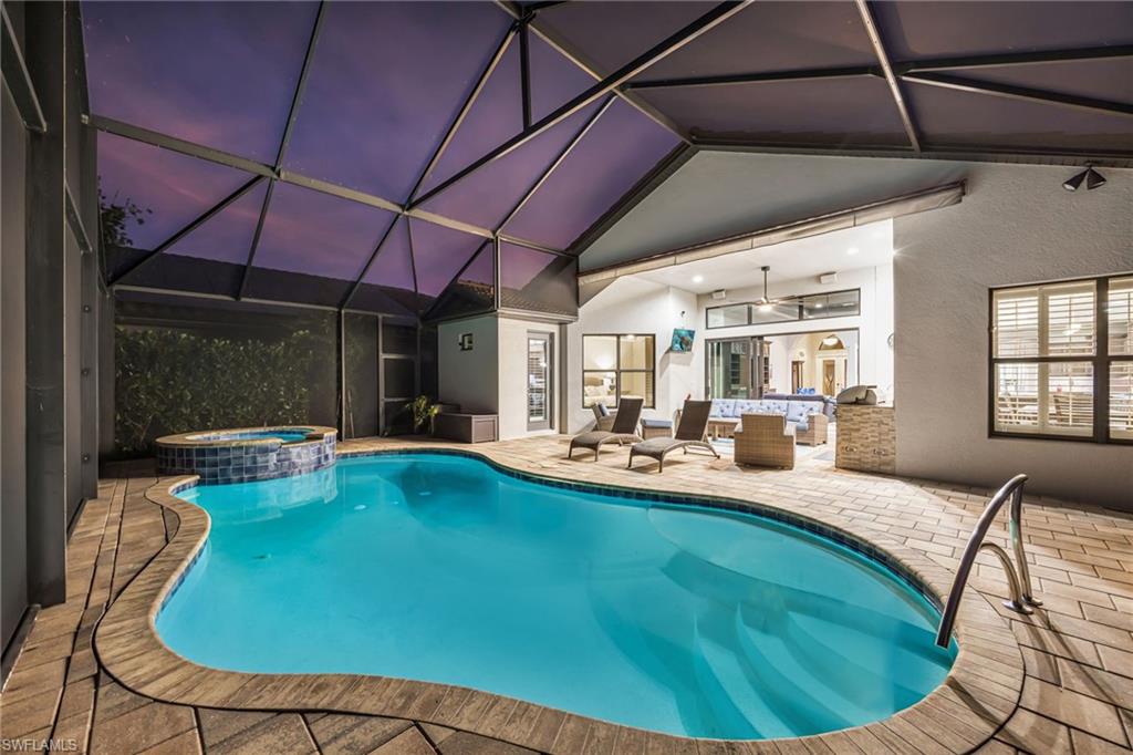 View of pool featuring glass enclosure, a patio area, a pool with connected hot tub, and an outdoor living space
