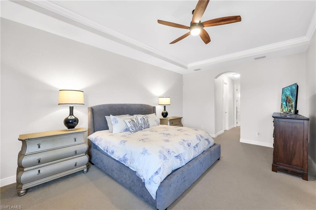 Carpeted bedroom featuring a ceiling fan, arched walkways, and a raised ceiling